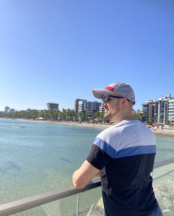 Homme souriant et regardant vers le soleil, avec la mer et Maceió, Brésil, en arrière-plan