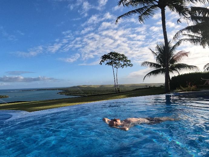 Photo d'un homme flottant dans la piscine au Brésil, détendu et profitant, avec vue sur la mer turquoise en arrière-plan et un ciel ensoleillé