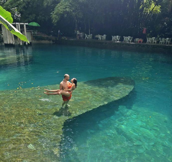 Homme portant une femme dans ses bras, à moitié immergés dans une eau clair et limpide au Brésil